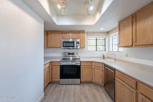 kitchen featuring appliances with stainless steel finishes, light hardwood / wood-style floors, rail lighting, sink, and a raised ceiling