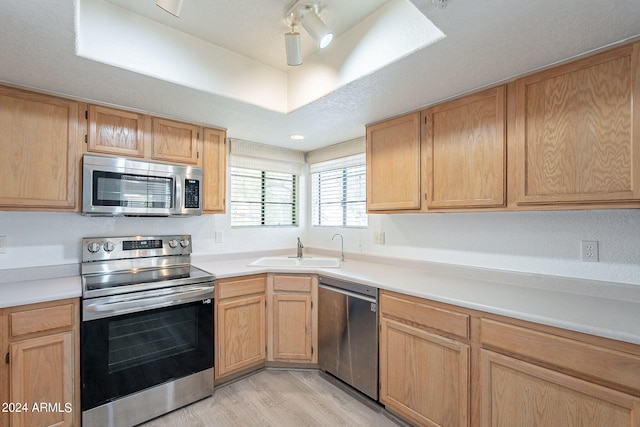 kitchen with sink, stainless steel appliances, light brown cabinets, and light hardwood / wood-style flooring