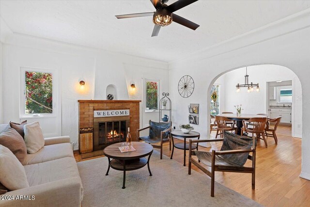 living room featuring a fireplace, light wood-type flooring, and ceiling fan with notable chandelier