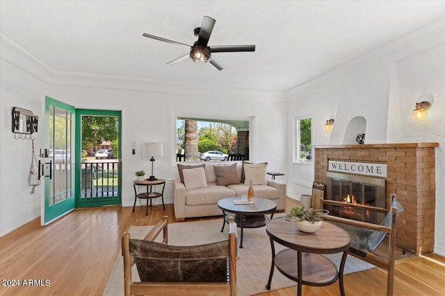 living room featuring crown molding, light hardwood / wood-style flooring, ceiling fan, and a fireplace