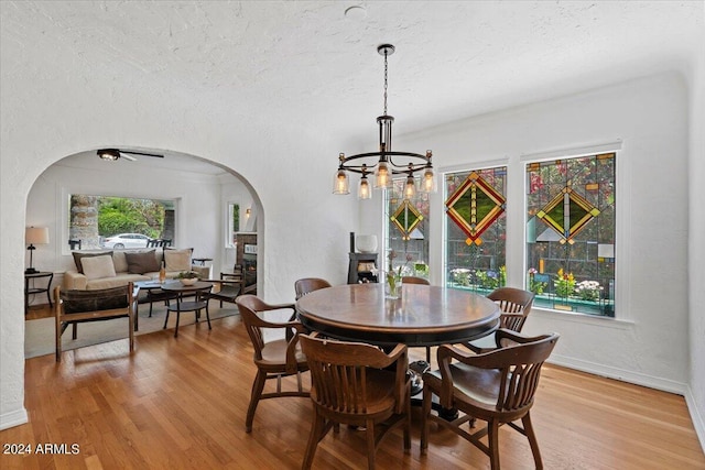 dining area featuring arched walkways, a notable chandelier, light wood-style flooring, and a textured ceiling