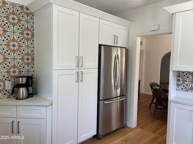 kitchen featuring light wood-style flooring, arched walkways, freestanding refrigerator, white cabinetry, and backsplash