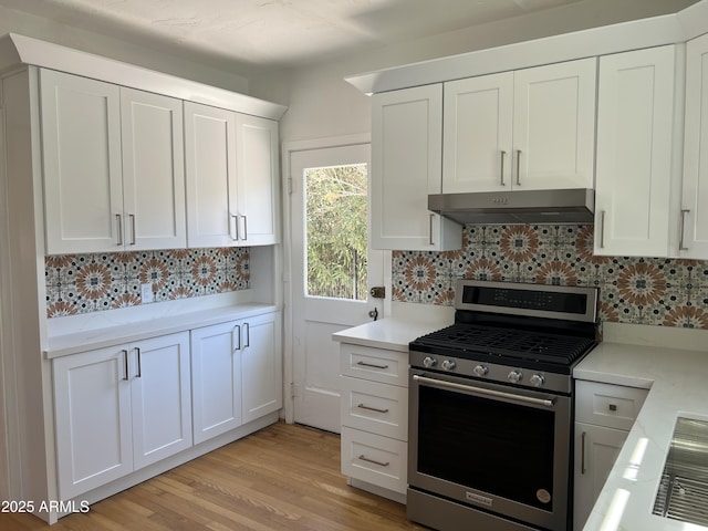 kitchen featuring under cabinet range hood, backsplash, stainless steel gas range oven, and light countertops