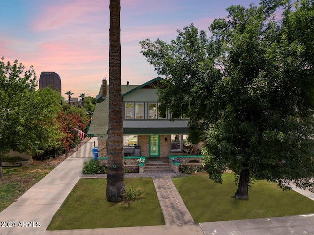 view of front facade featuring brick siding, a lawn, a porch, and a chimney