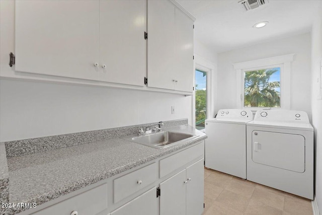 washroom with cabinets, washing machine and clothes dryer, and sink