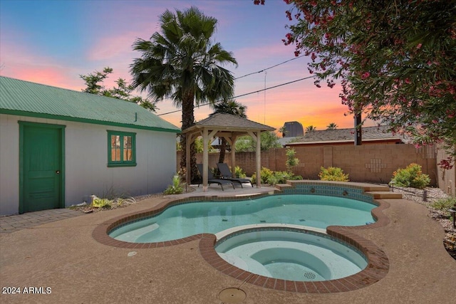 pool at dusk with a gazebo, a patio area, a pool with connected hot tub, and a fenced backyard