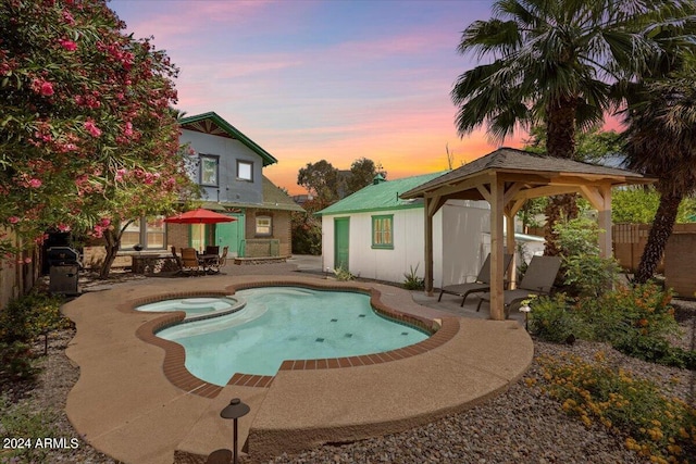 pool at dusk featuring a patio area, an in ground hot tub, and a gazebo