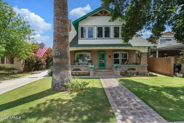 view of front of house with brick siding, a porch, a front yard, and roof with shingles