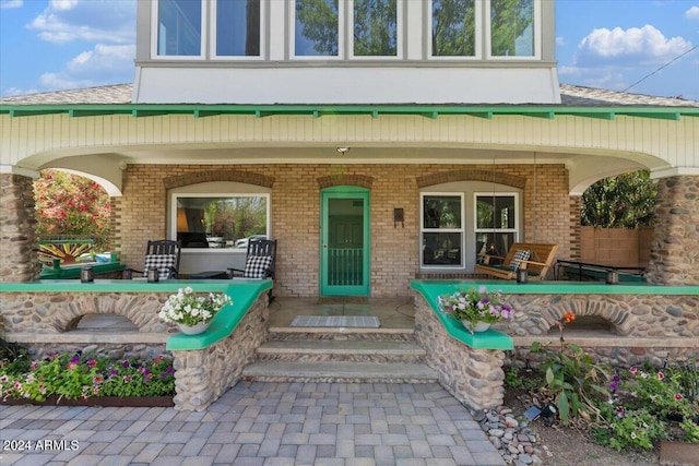 view of exterior entry with brick siding, covered porch, and stucco siding