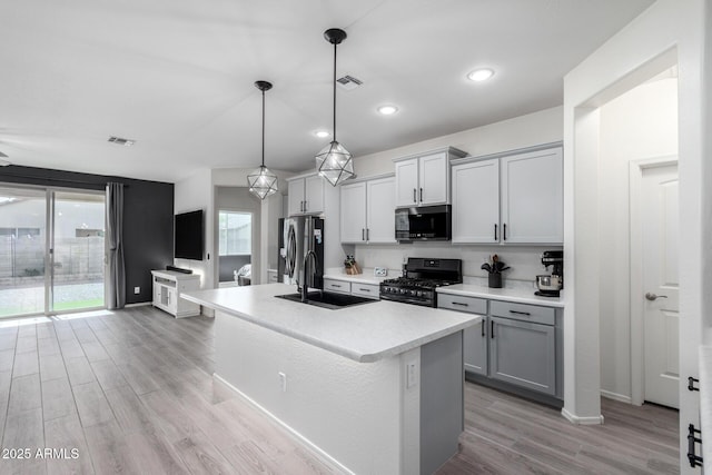 kitchen featuring sink, gray cabinetry, an island with sink, pendant lighting, and black appliances