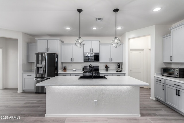 kitchen featuring stainless steel appliances, decorative light fixtures, sink, and a center island with sink