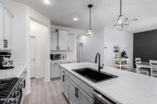 kitchen featuring decorative light fixtures, tasteful backsplash, sink, stainless steel range with gas stovetop, and light hardwood / wood-style flooring