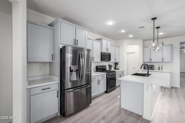 kitchen featuring sink, hanging light fixtures, light hardwood / wood-style floors, black appliances, and an island with sink