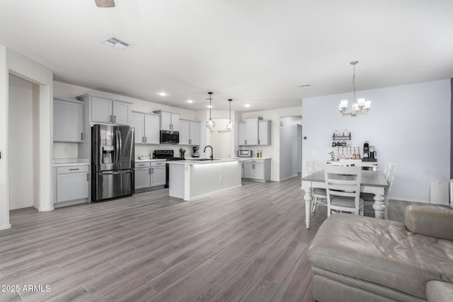 kitchen with stainless steel appliances, an island with sink, hanging light fixtures, and gray cabinets