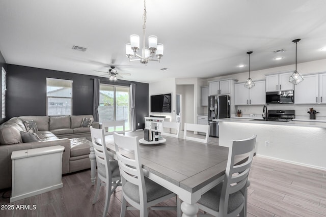 dining area with sink, ceiling fan with notable chandelier, and light hardwood / wood-style flooring