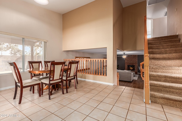 dining area with a high ceiling, ceiling fan, light hardwood / wood-style floors, and a brick fireplace