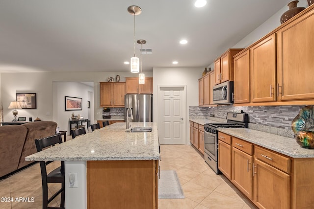 kitchen with sink, decorative light fixtures, a kitchen breakfast bar, stainless steel appliances, and a kitchen island with sink