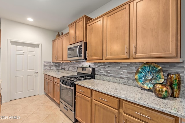 kitchen with tasteful backsplash, light stone countertops, appliances with stainless steel finishes, and light tile patterned floors