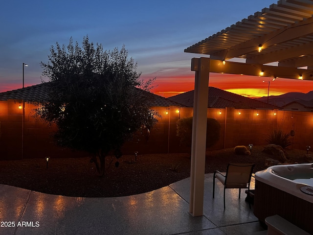 patio terrace at dusk with a hot tub and a pergola