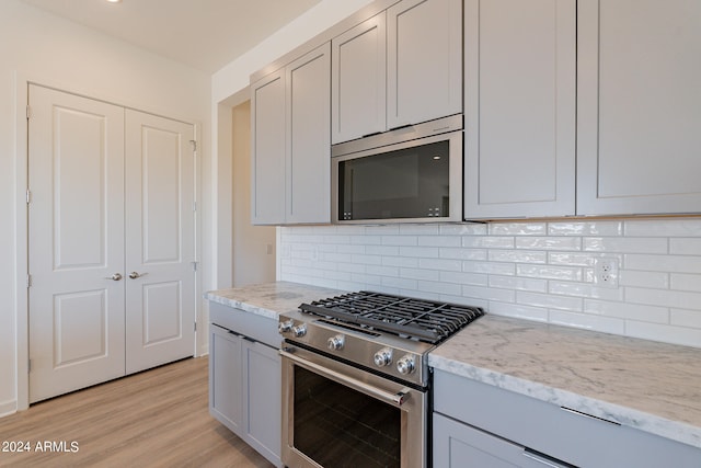 kitchen with appliances with stainless steel finishes, backsplash, light stone counters, and light hardwood / wood-style flooring