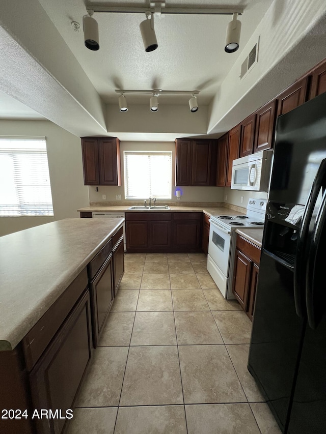 kitchen with sink, a raised ceiling, a textured ceiling, white appliances, and light tile patterned flooring