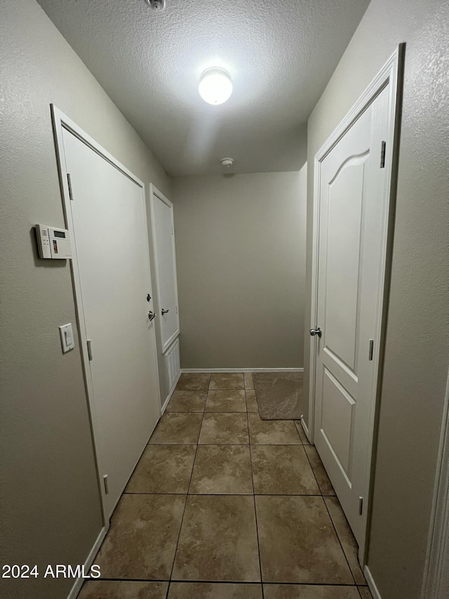 hall with a textured ceiling and dark tile patterned flooring