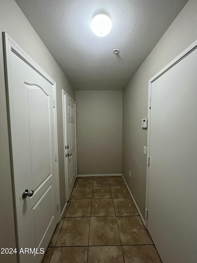 corridor featuring a textured ceiling and dark tile patterned flooring