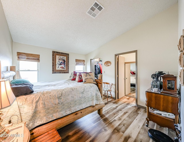 bedroom with vaulted ceiling, a textured ceiling, multiple windows, and wood finished floors