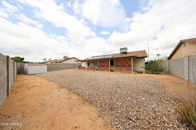 back of property featuring a shed, a fenced backyard, an outdoor structure, a patio area, and roof mounted solar panels