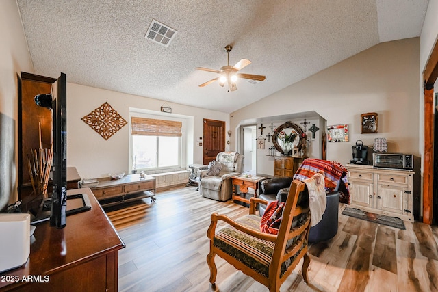 living room featuring vaulted ceiling, a ceiling fan, a textured ceiling, and wood finished floors