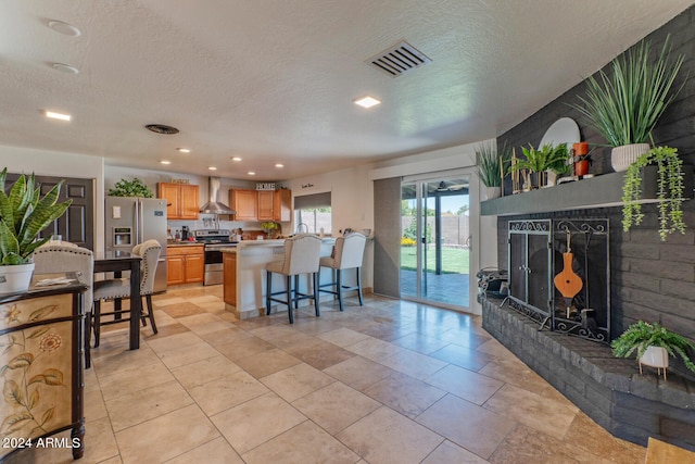 kitchen with a kitchen bar, kitchen peninsula, stainless steel appliances, a textured ceiling, and wall chimney exhaust hood