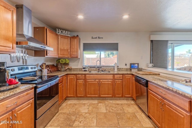 kitchen featuring wall chimney exhaust hood, sink, appliances with stainless steel finishes, kitchen peninsula, and light stone countertops