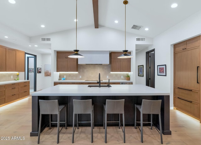 kitchen with sink, vaulted ceiling with beams, hanging light fixtures, a spacious island, and light wood-type flooring