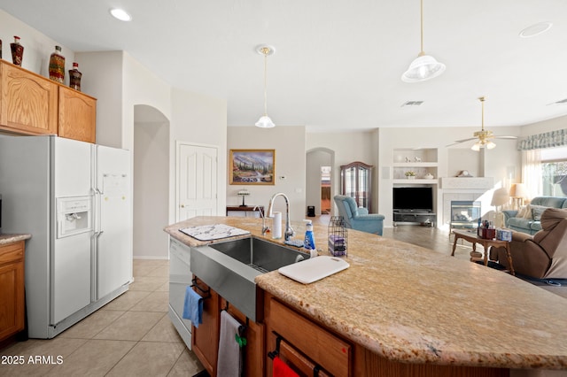 kitchen featuring visible vents, an island with sink, arched walkways, a sink, and white fridge with ice dispenser