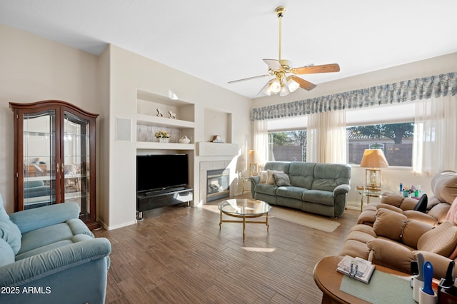 living room with wood finished floors, a fireplace, baseboards, built in shelves, and a ceiling fan