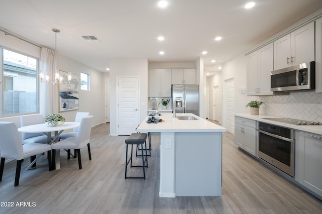 kitchen featuring a kitchen island with sink, hanging light fixtures, decorative backsplash, and appliances with stainless steel finishes