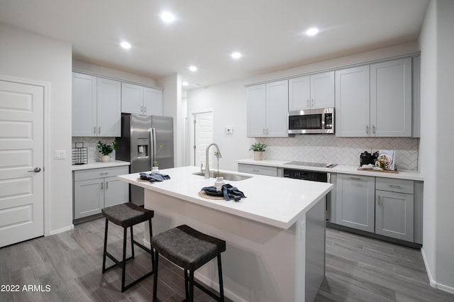 kitchen with gray cabinets, an island with sink, sink, a breakfast bar area, and stainless steel appliances