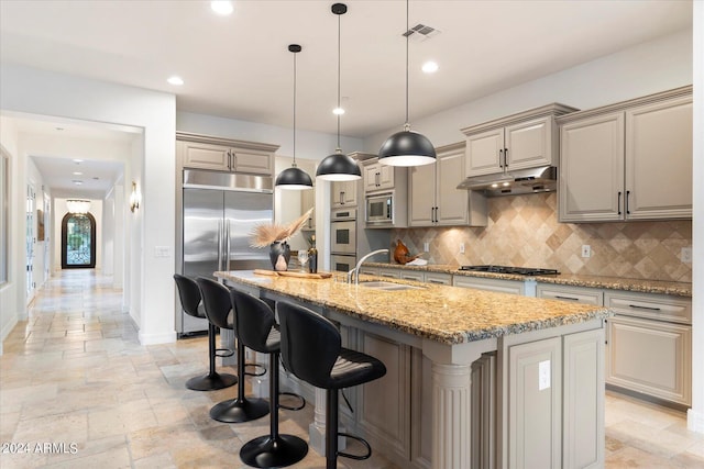 kitchen featuring stone tile floors, visible vents, a sink, built in appliances, and under cabinet range hood