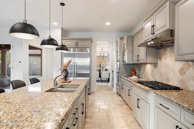 kitchen with tasteful backsplash, stone tile flooring, a sink, black gas stovetop, and under cabinet range hood