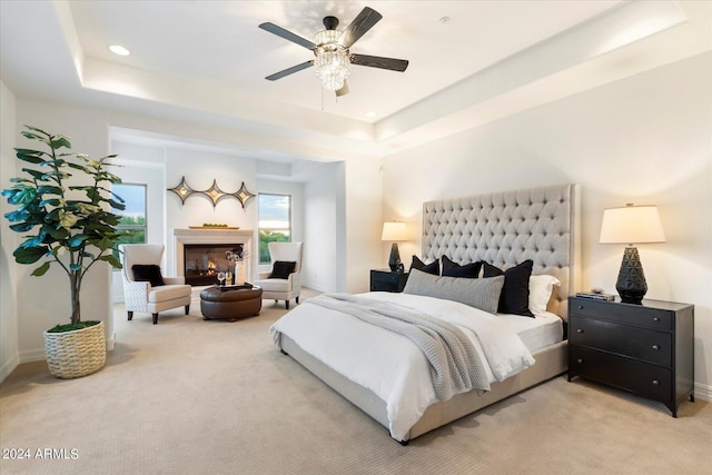 bedroom with a lit fireplace, a raised ceiling, and light colored carpet