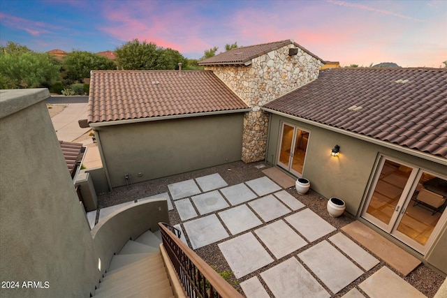 back of property with stone siding, a tile roof, french doors, a patio area, and stucco siding