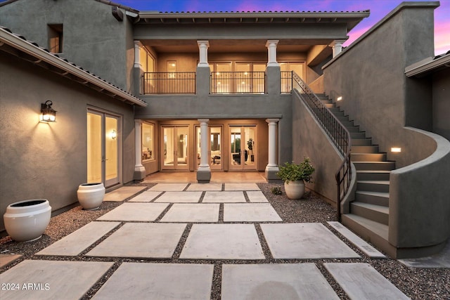 back of house at dusk with stairs, french doors, a balcony, and stucco siding