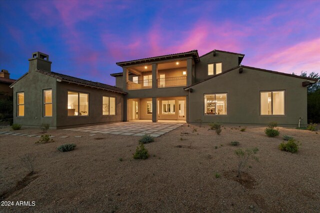 back of property at dusk featuring a patio area, a balcony, and stucco siding