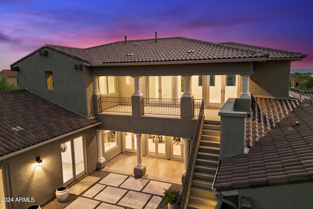 back of house featuring a patio, a balcony, a tile roof, french doors, and stucco siding