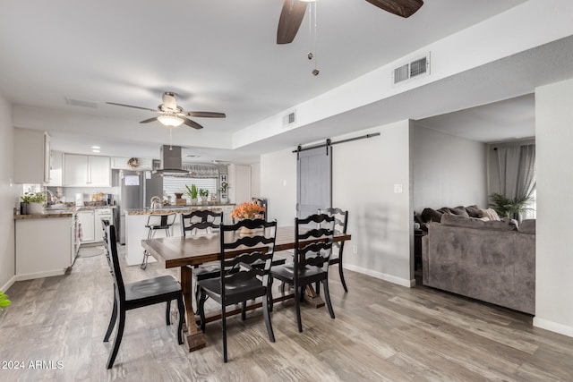 dining area featuring a barn door, ceiling fan, and light hardwood / wood-style flooring