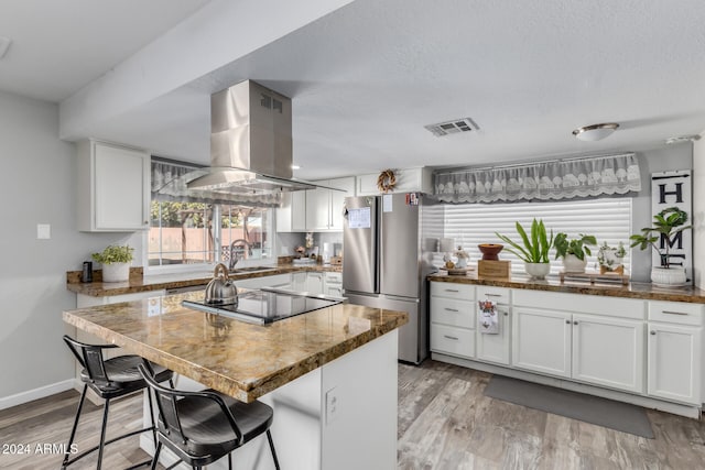 kitchen with white cabinets, stainless steel fridge, light hardwood / wood-style floors, a kitchen island, and island exhaust hood