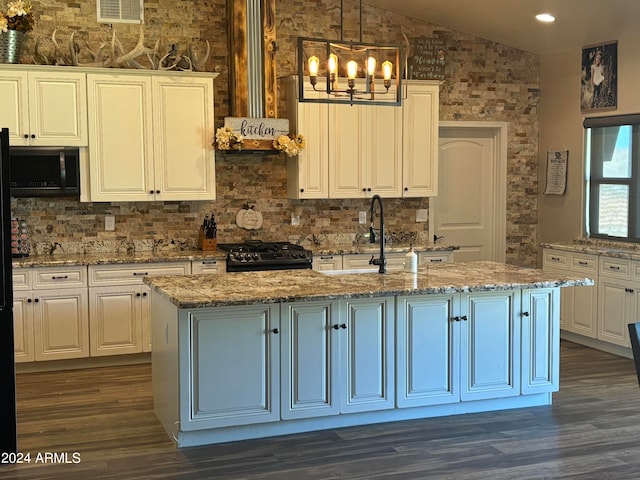 kitchen featuring black stove, lofted ceiling, hanging light fixtures, a kitchen island with sink, and light stone countertops