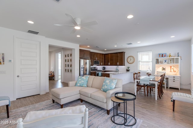 living room with ceiling fan, light hardwood / wood-style floors, and sink