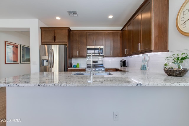 kitchen with sink, light stone countertops, tasteful backsplash, kitchen peninsula, and stainless steel appliances