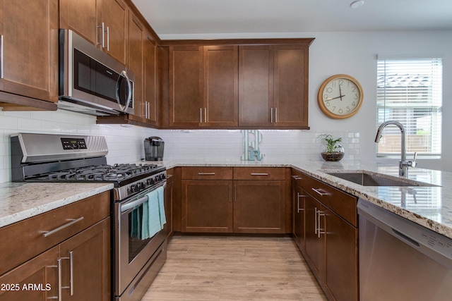 kitchen featuring backsplash, sink, light wood-type flooring, light stone countertops, and appliances with stainless steel finishes